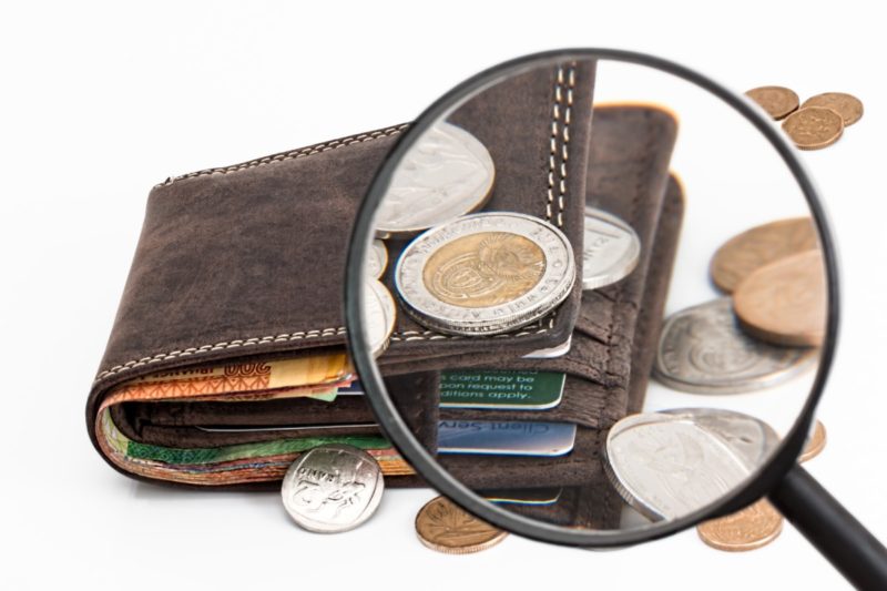 虫眼鏡でコインの溢れる財布を見ている画像